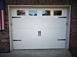 A white garage door with black hinges is sitting in front of a brick building.