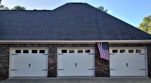 A garage with three white garage doors and an american flag hanging from the roof.