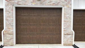 A brown garage door is sitting in front of a brick building.