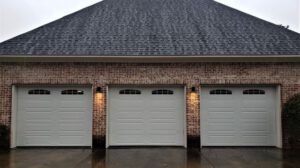 Three white garage doors are lined up in front of a brick house.