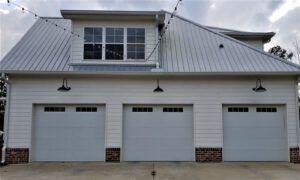 A white house with three garage doors and a metal roof.