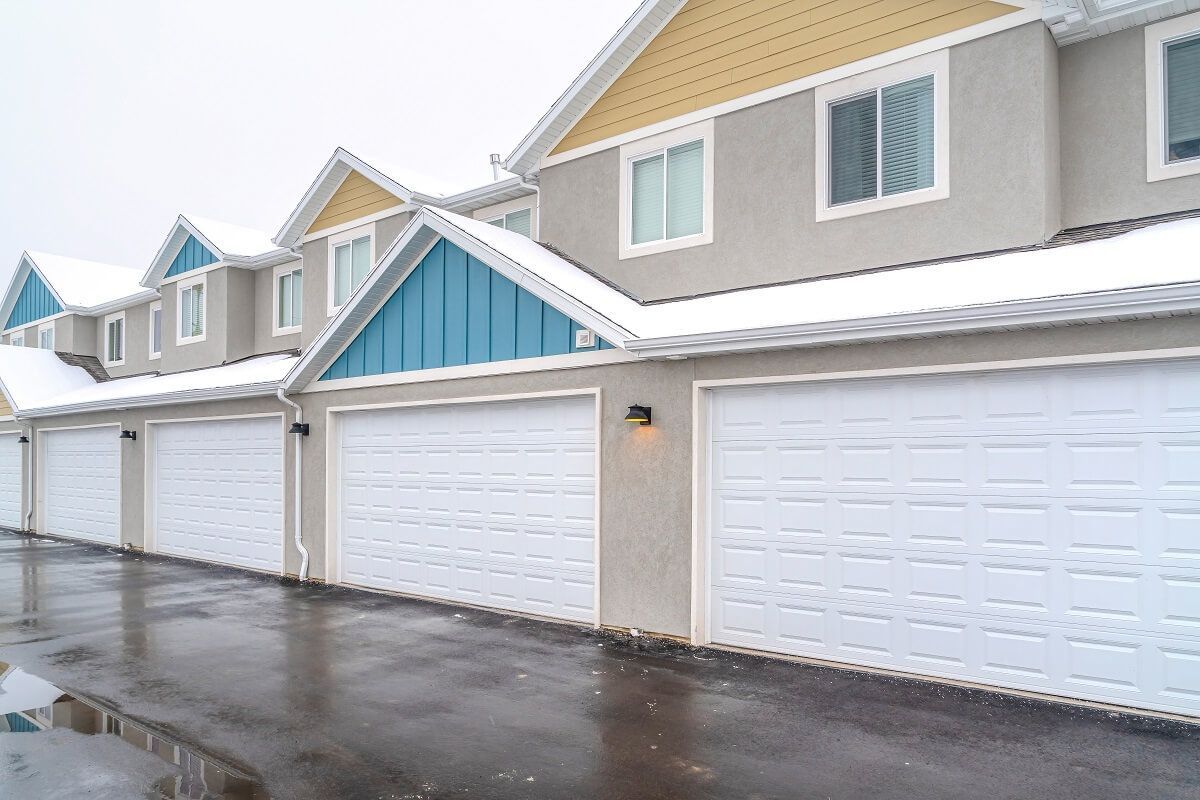Row of modern townhouses with white garage doors and snow on the roofs.