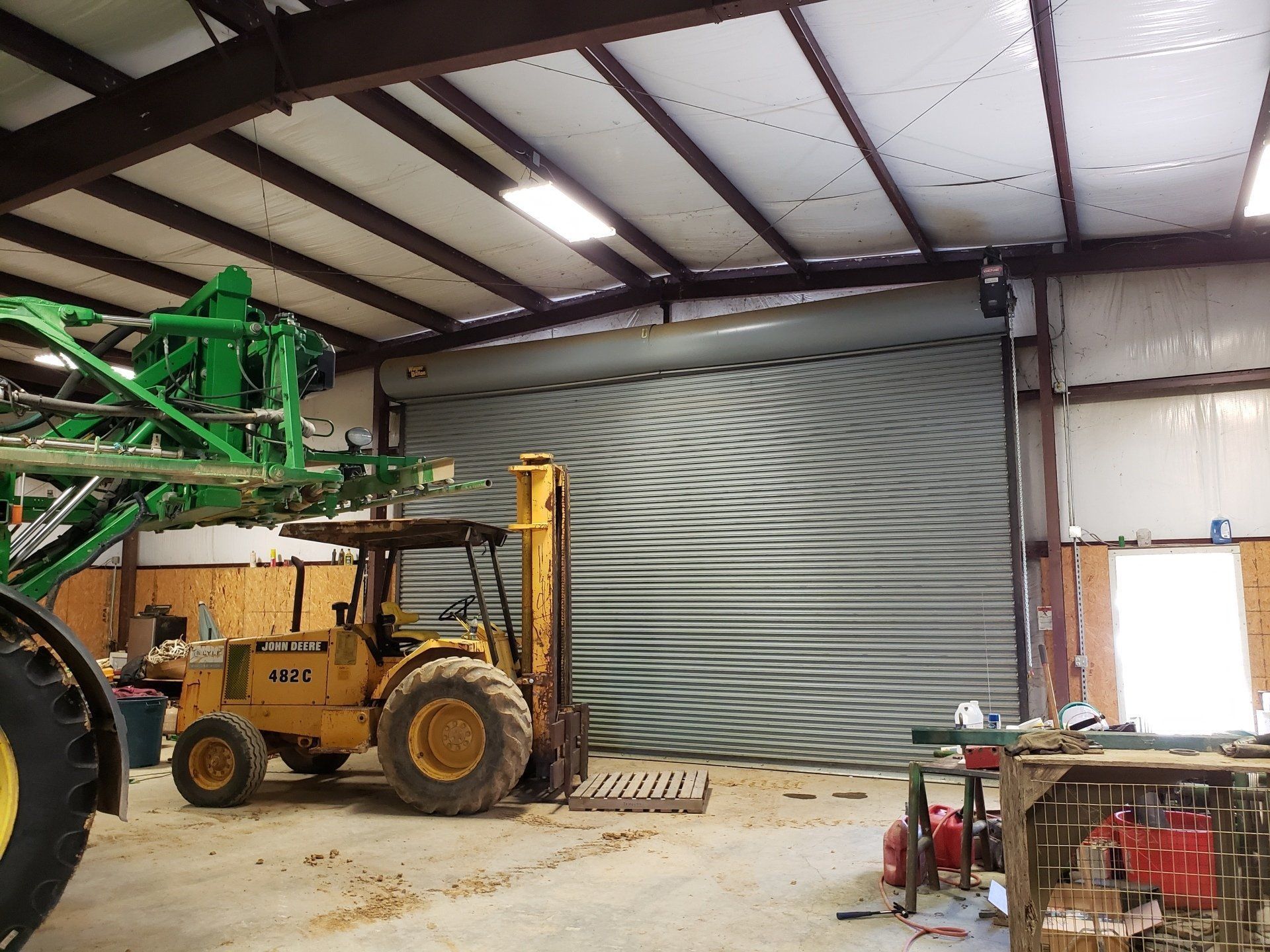 A yellow tractor is parked in a garage next to a green sprayer.