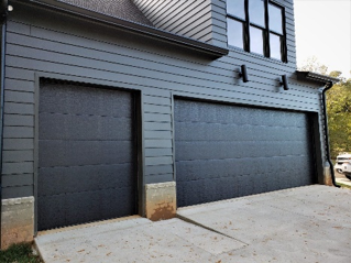 Modern home exterior featuring two dark garage doors with a clean driveway and siding.