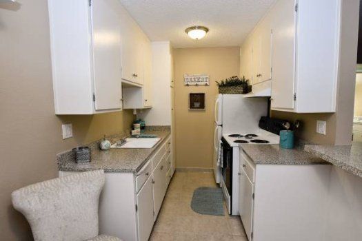 Narrow white kitchen with countertops, stove, sink, and a refrigerator under warm ceiling light