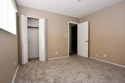Empty beige bedroom with carpet, closet doors, and an open doorway