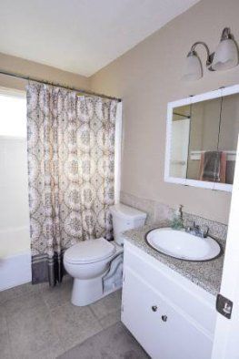 Small bathroom with toilet, sink vanity, mirror, shower curtain, and wall lights.
