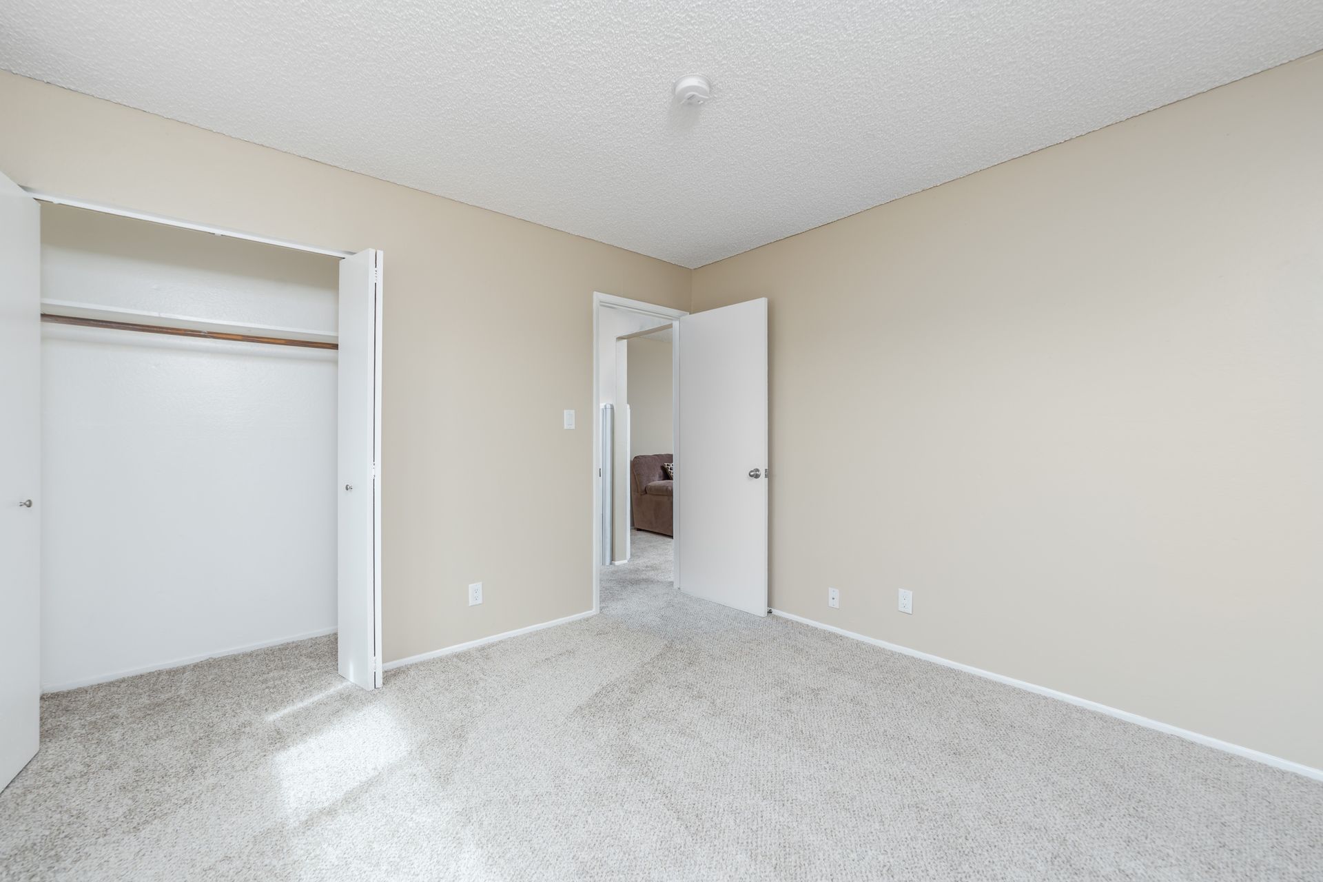 Empty beige bedroom with open closet and doorway, light carpet, and white trim