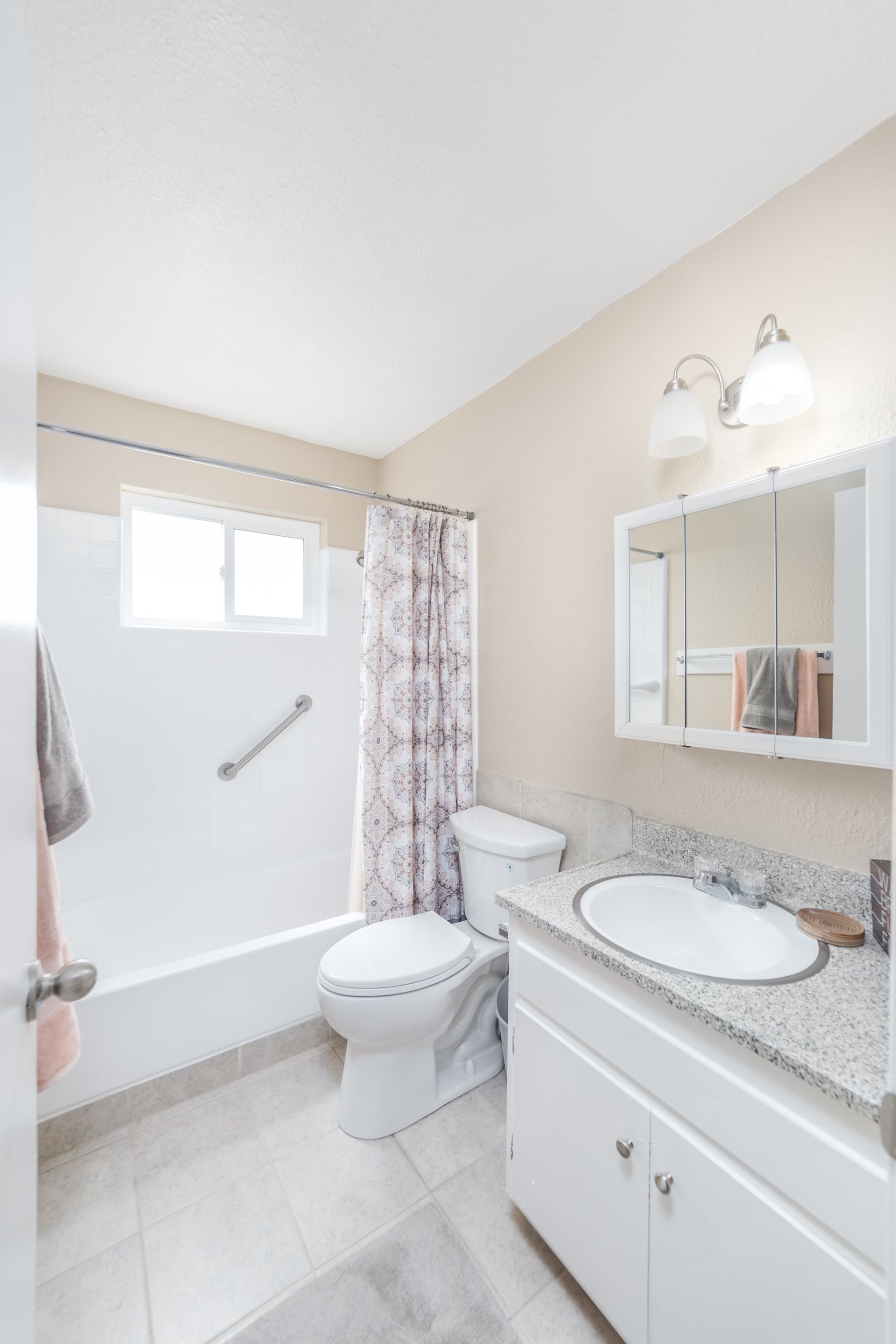 Bright bathroom with a white tub, toilet, vanity, and mirrored cabinet.