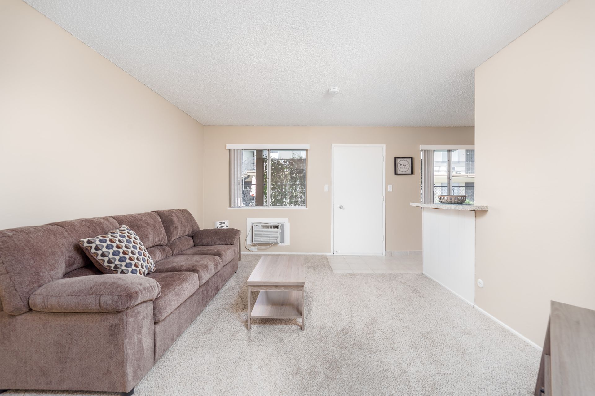 Bright living room with a gray couch, coffee table, carpet, and open view to a kitchen area
