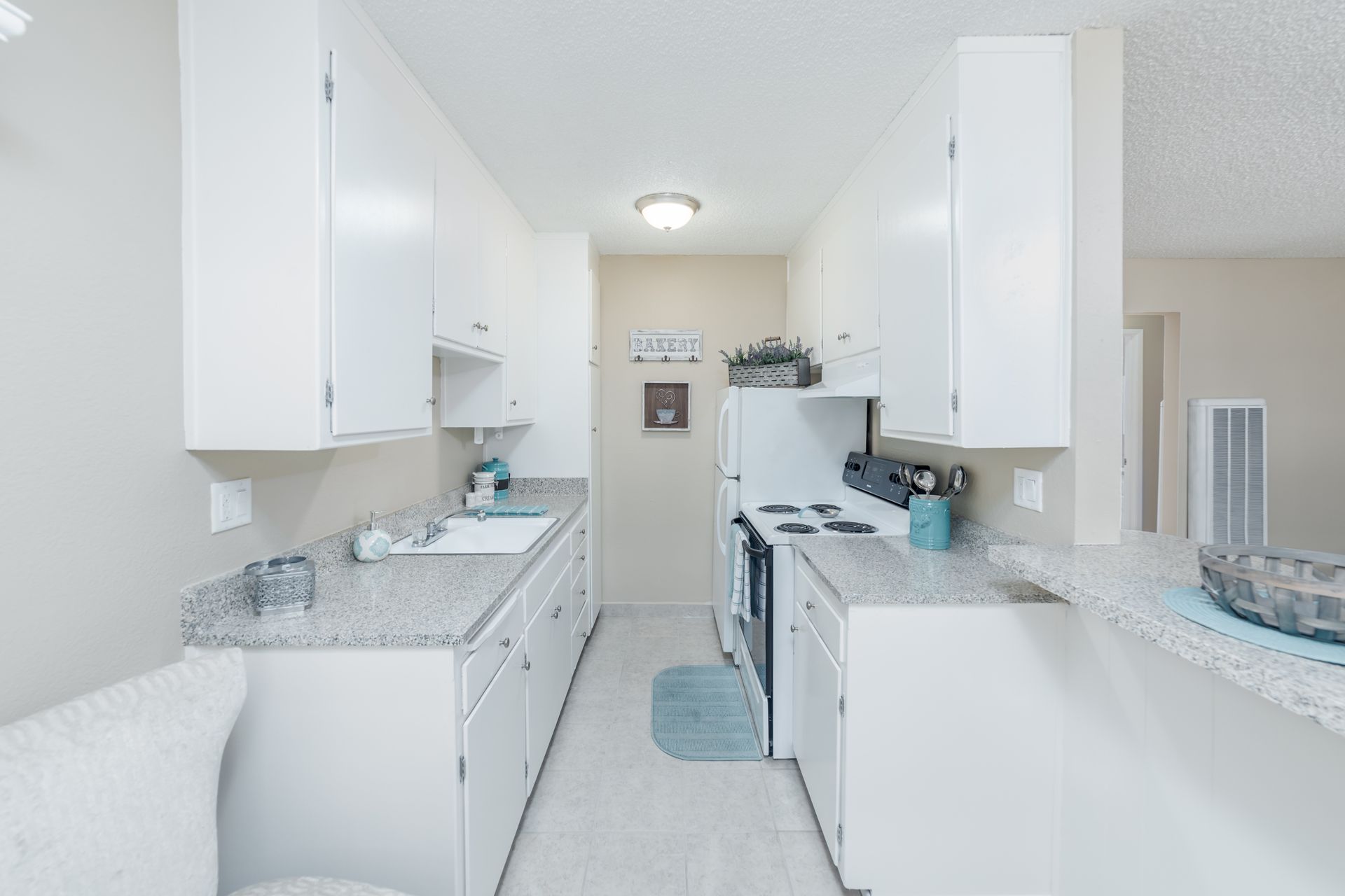 Bright white galley kitchen with granite counters, white cabinets, and a blue floor mat