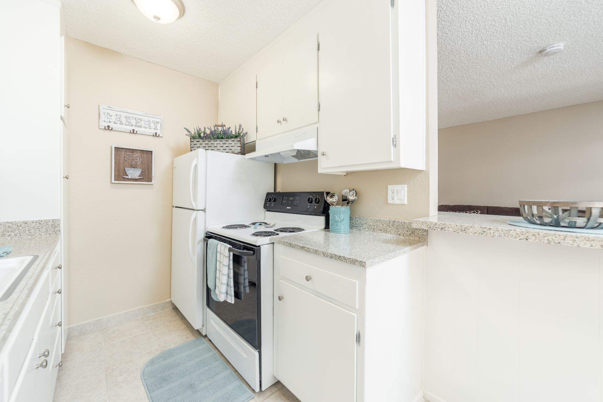 Small white kitchen with stove, fridge, cabinets, and granite countertops in a bright apartment