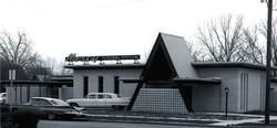 Black and white photo of a 1950s-style Mercury car dealership building with an A-frame entrance and vintage cars.