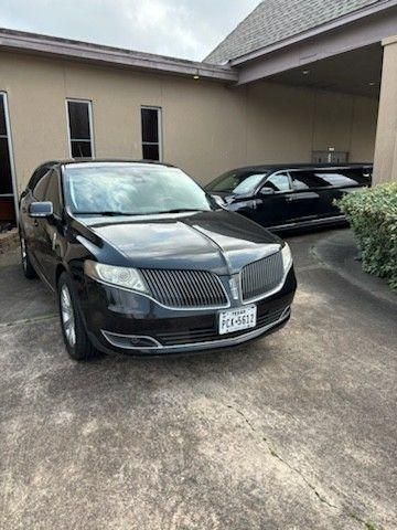 A black Lincoln MKT and a black limousine parked on a concrete driveway in front of a building.