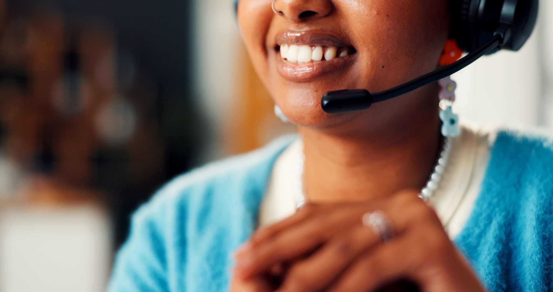 A person wearing a headset and blue cardigan smiles while working in an office setting.