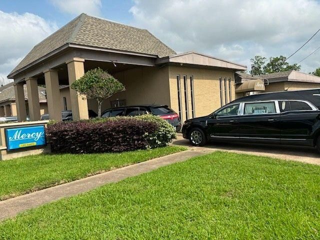 A black hearse is parked under the porte-cochère of a tan building with a sign that reads 