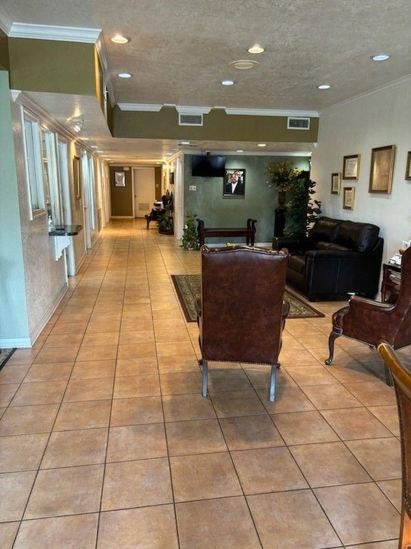 A spacious waiting room with tan tile floors, leather chairs, a couch, framed pictures, and a hallway in the background.