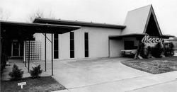 A black-and-white photo of a mid-century building with a sharp, triangular roof entrance labeled 