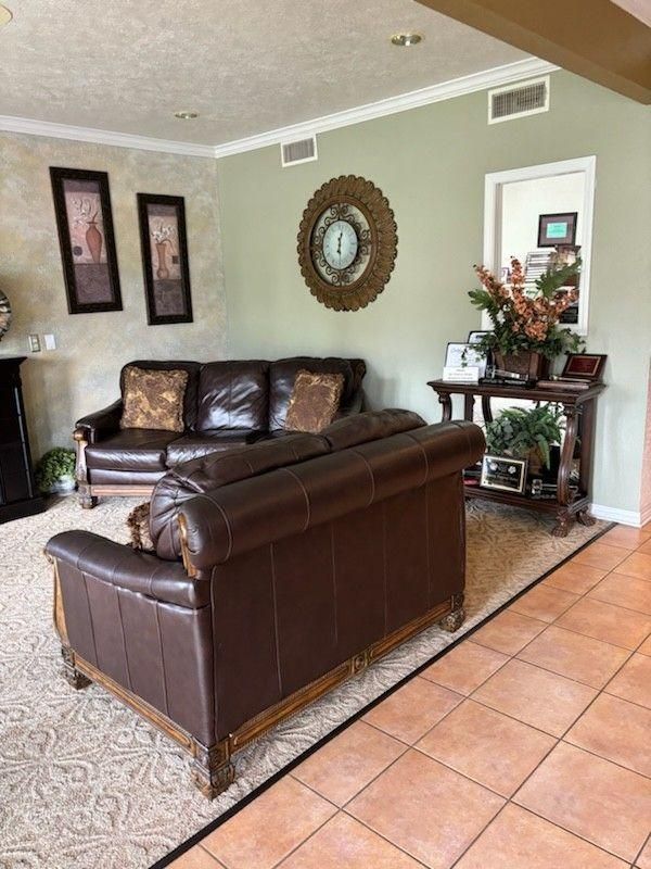 A living room features two brown leather sofas on a rug next to a side table with decor, beneath a wall-mounted clock.
