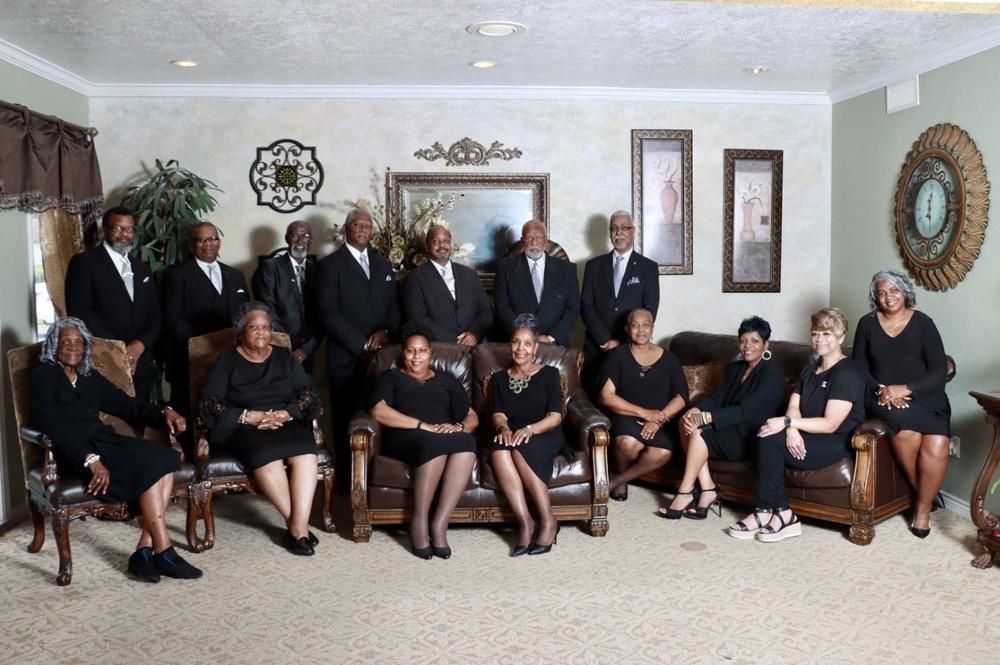 Group of people dressed in black formal attire posing for a formal portrait in a neutrally decorated indoor room.