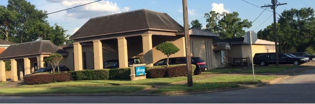 A tan single-story commercial building with a hip roof and a covered portico, situated on a landscaped corner lot.