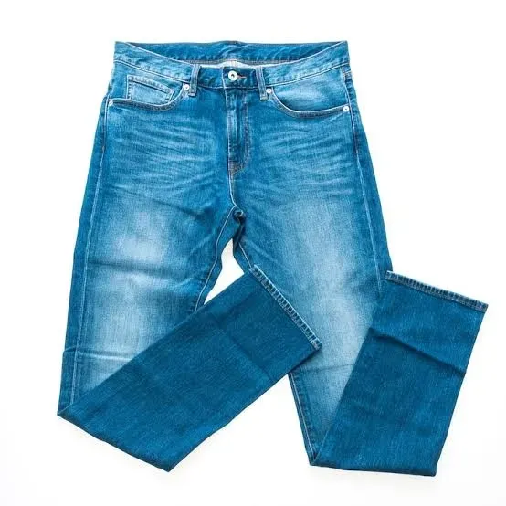 Unos pantalones vaqueros azules extendidos sobre un fondo blanco, con una pierna doblada sobre la otra.