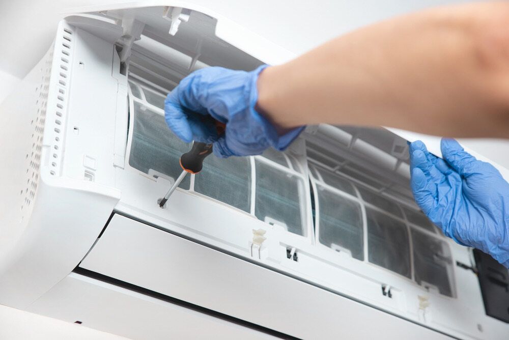 A Person Wearing Blue Gloves Is Fixing An Air Conditioner — RAFFBRO Electrical Solar & Air Conditioning In Wodonga, VIC