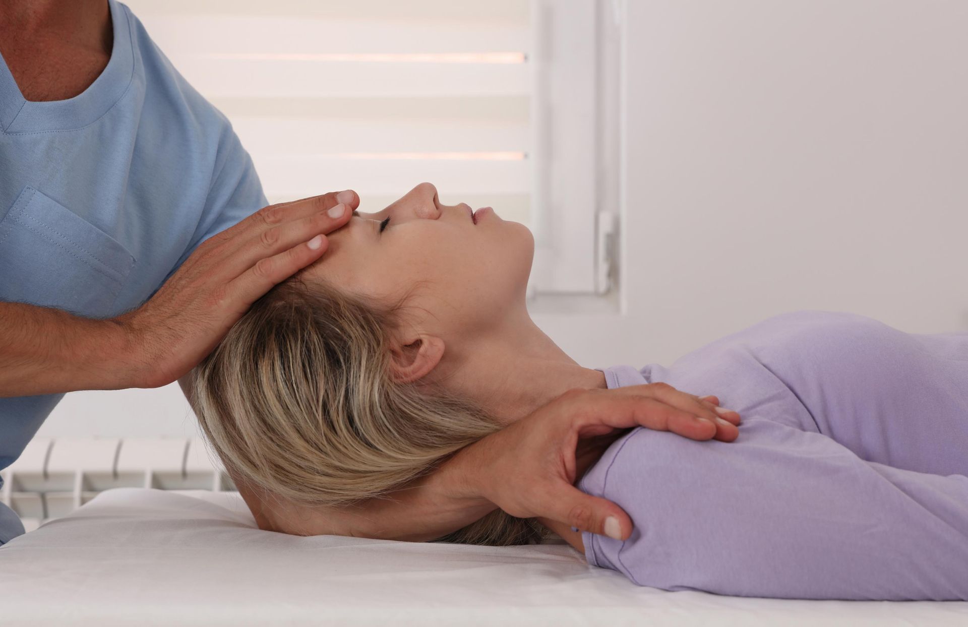Therapist performs a gentle neck adjustment on a woman lying on a treatment table