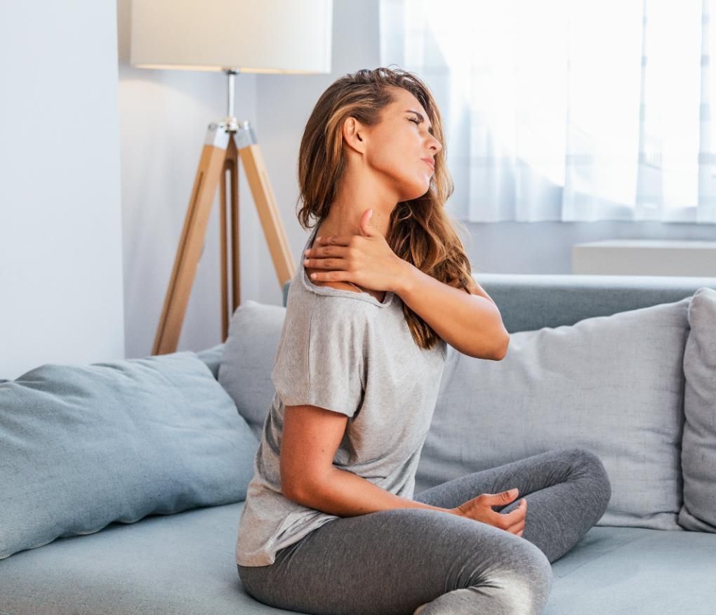 Person sitting on a couch, clutching their neck in pain in a bright living room