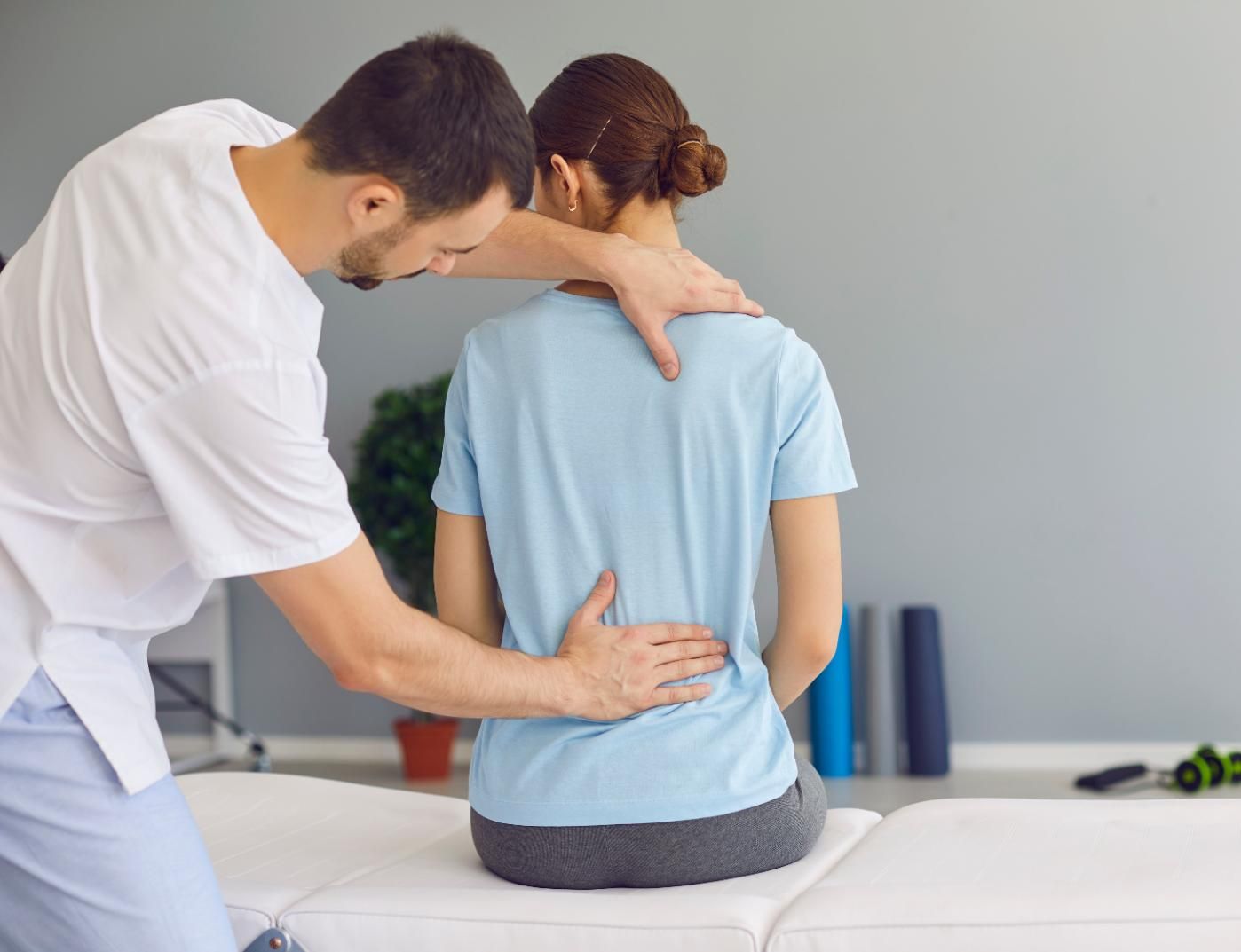 Physical therapist guiding a patient’s back during a treatment session in a clinic room