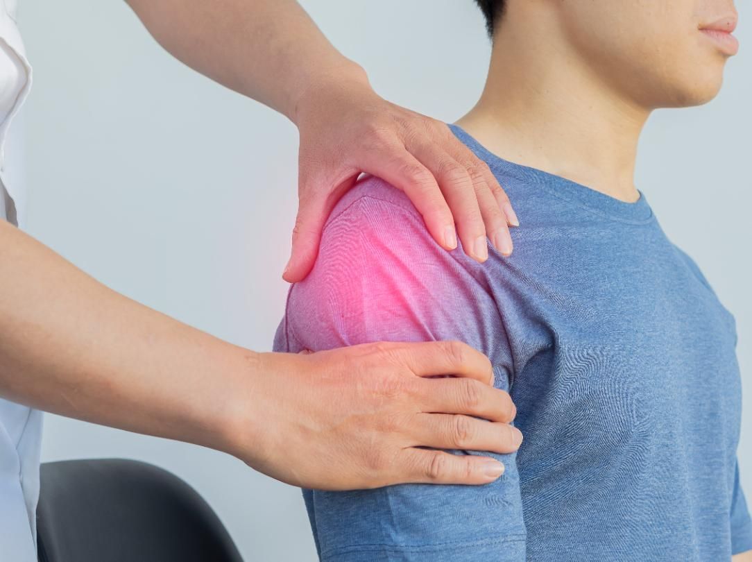 Therapist massaging a person’s shoulder, highlighting shoulder pain in pink