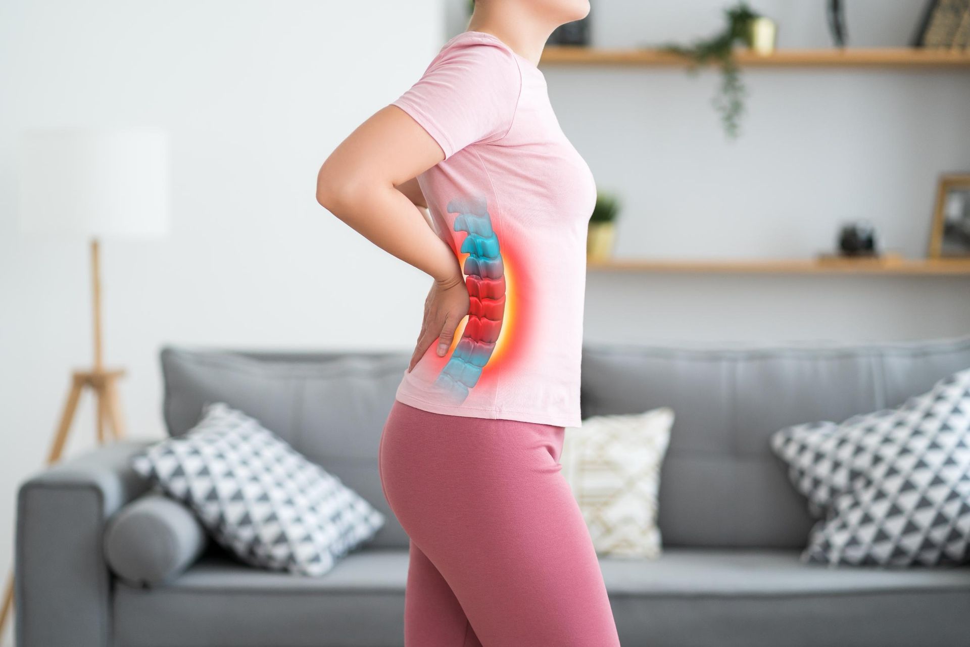 Person in pink shirt and leggings holding lower back in a living room, showing back pain