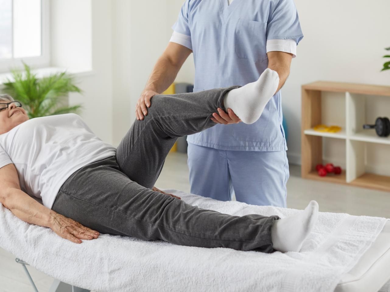 Physical therapist stretching a patient’s leg on a treatment table in a bright clinic room