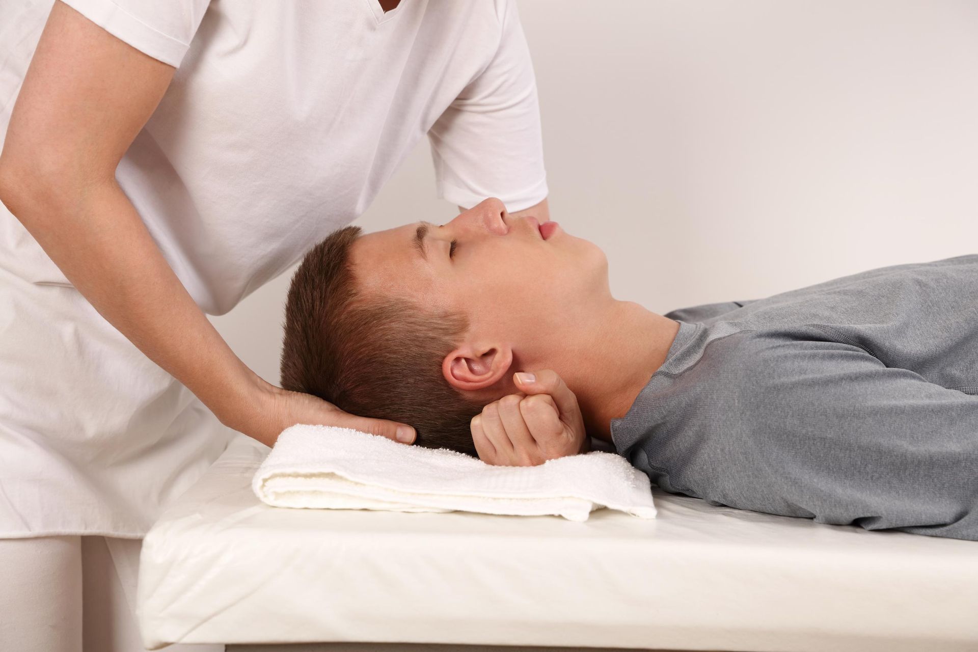 Massage therapist adjusting a man's neck as he lies on a treatment table