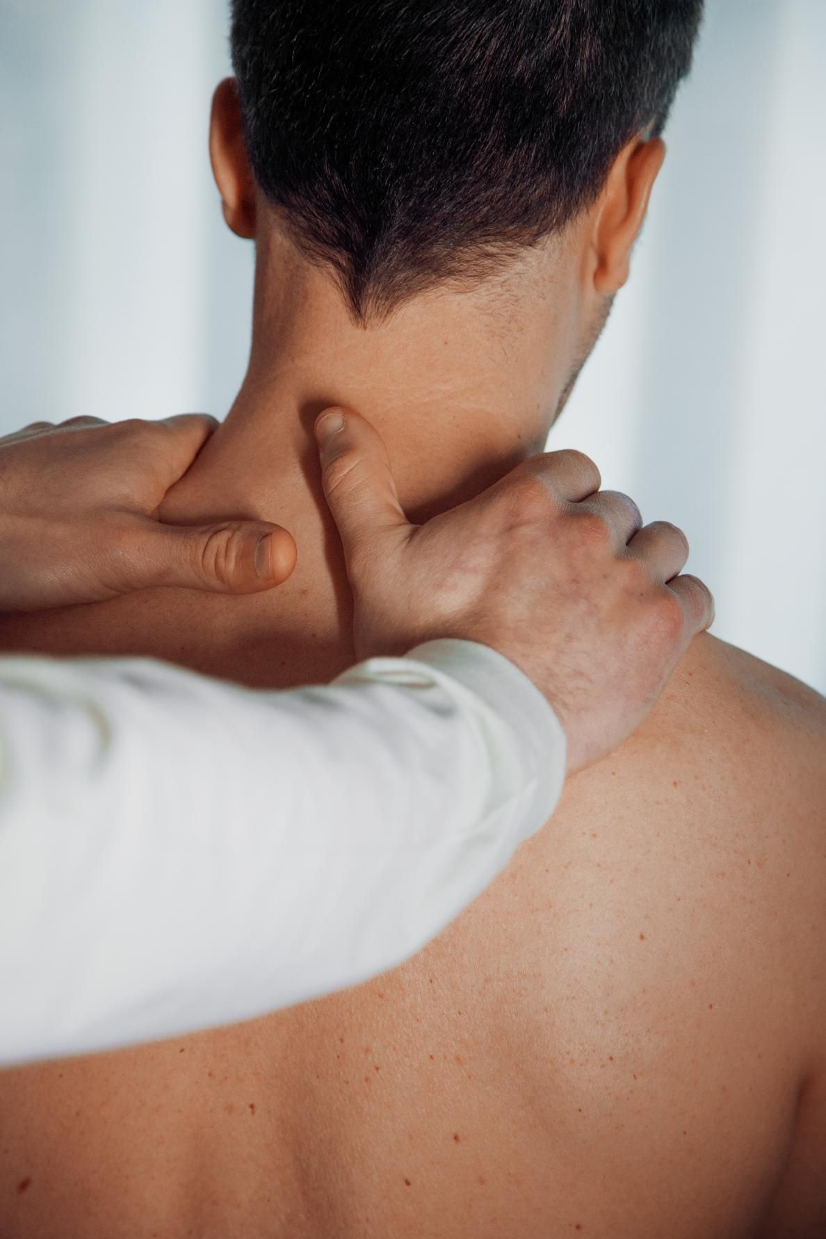Hands massage the back of a person's neck and shoulders from behind.