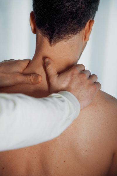 Hands massage the back of a person's neck and shoulders from behind.