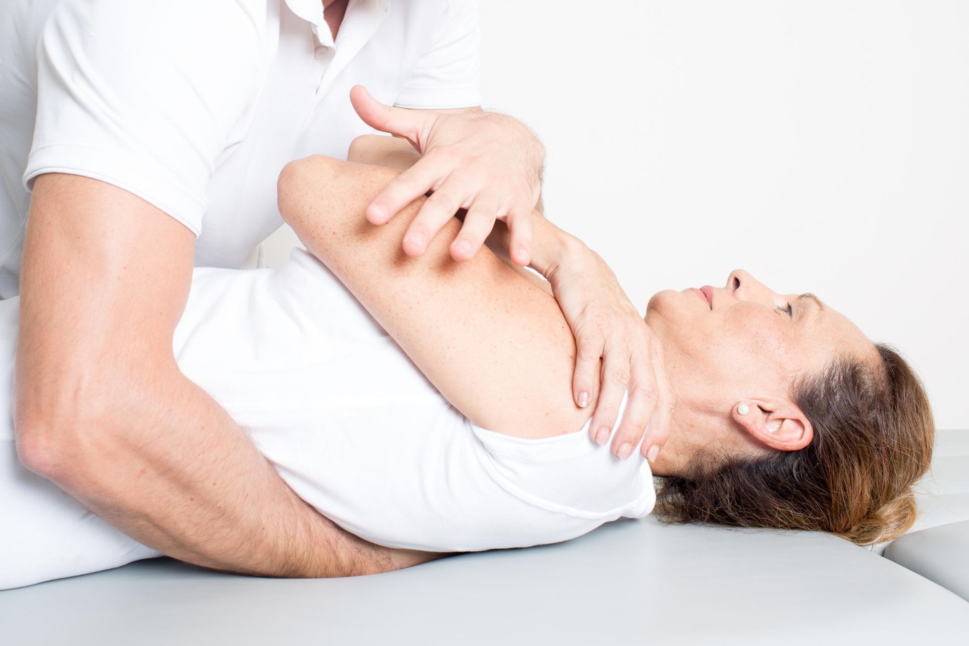 Physical therapist stretching a patient’s arm on a white treatment table