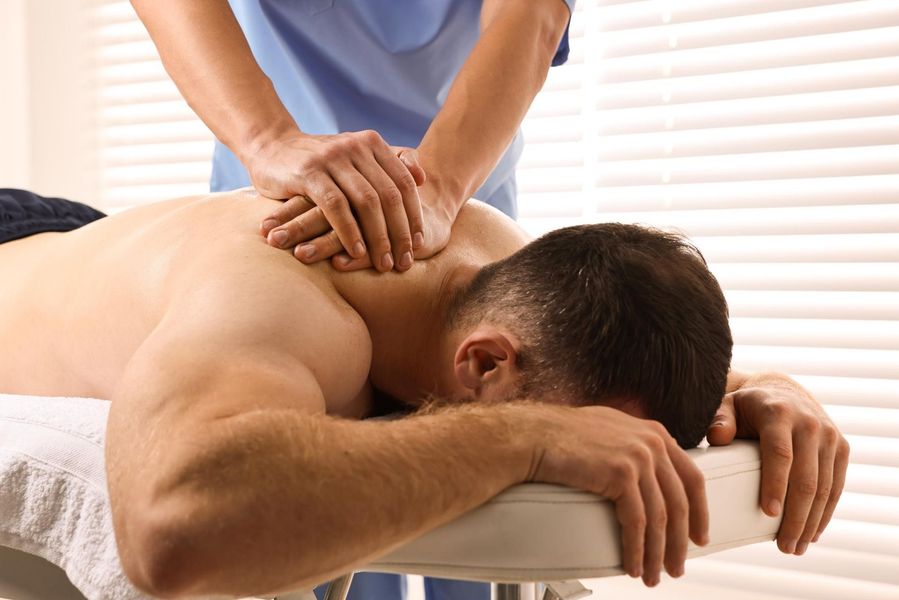 Massage therapist pressing a man's back on a massage table in a bright room