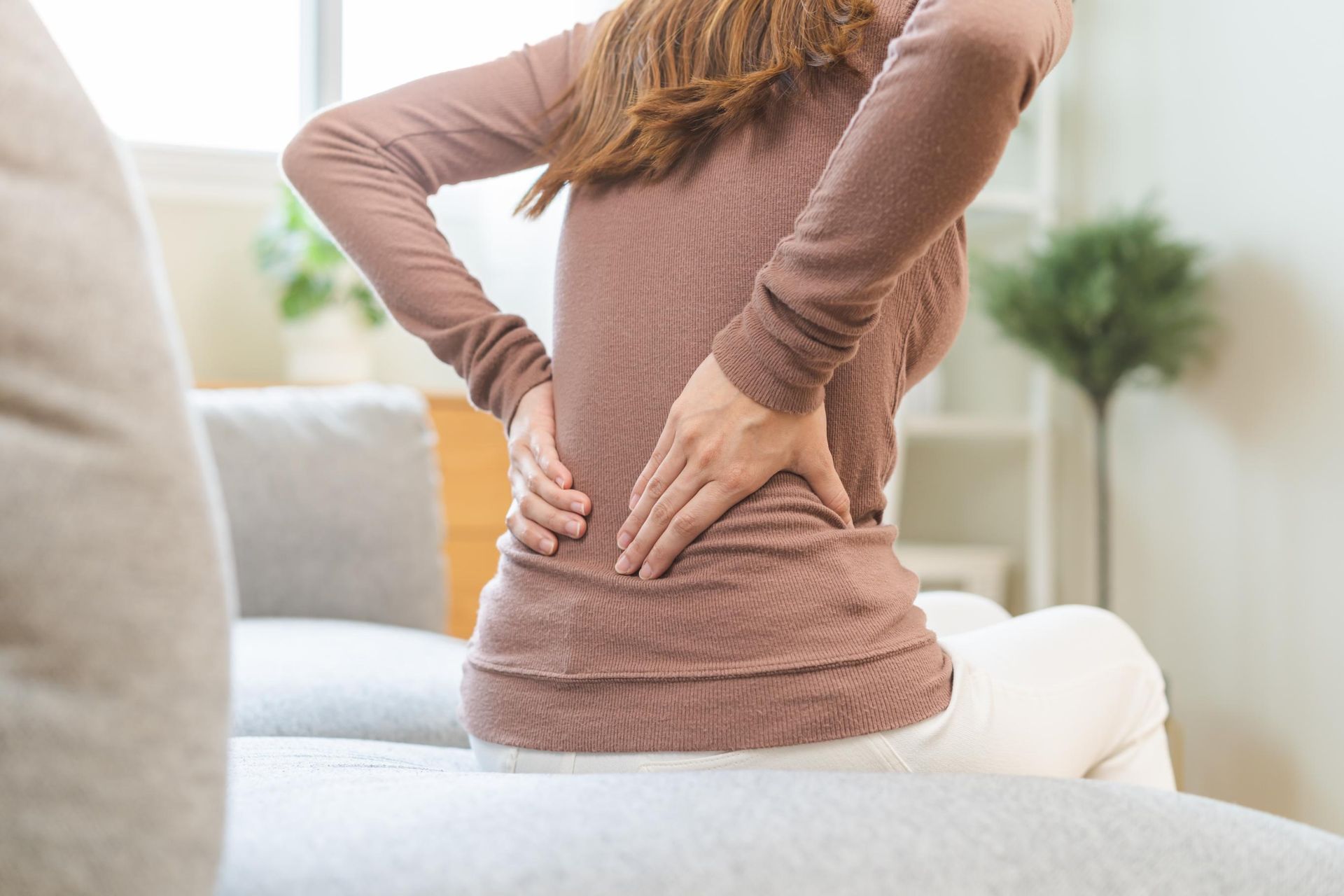 Person holding lower back while sitting on a couch indoors