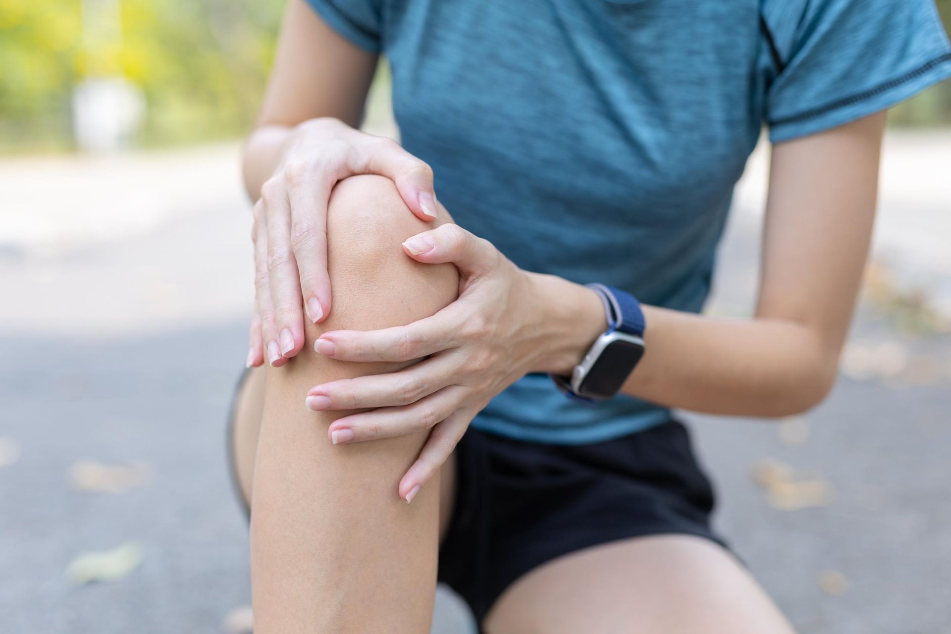 Person holding a bent knee outdoors, suggesting knee pain or injury.