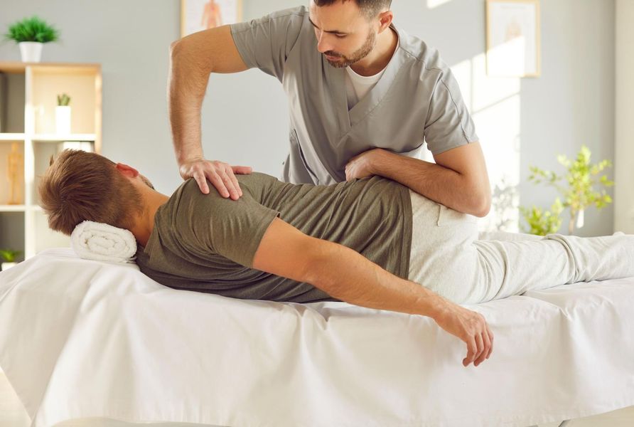 Therapist assisting a client with a back stretch on a treatment table in a bright clinic room