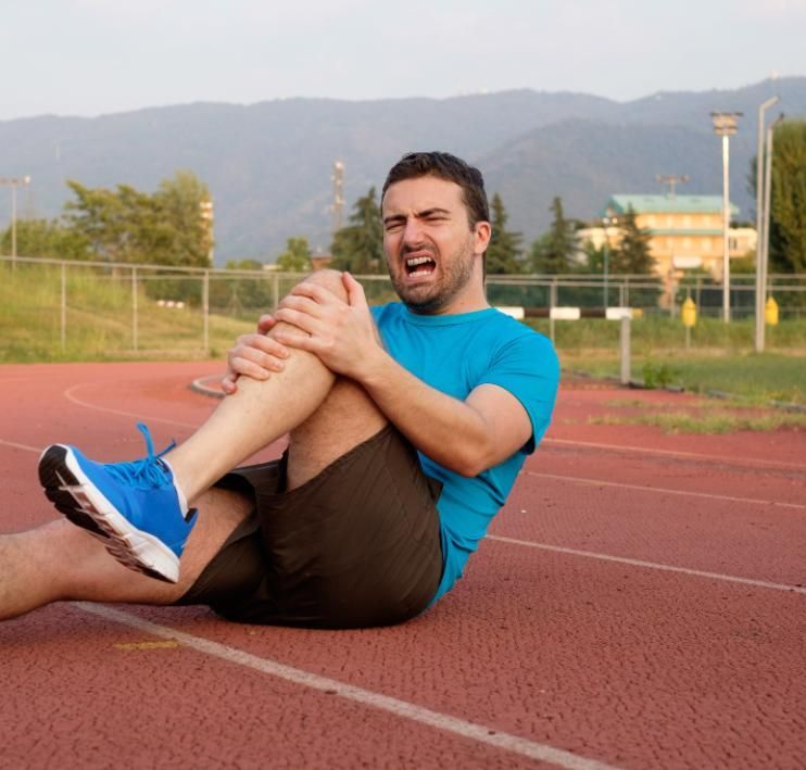 Man in blue shirt clutching his leg and grimacing on a running track outdoors