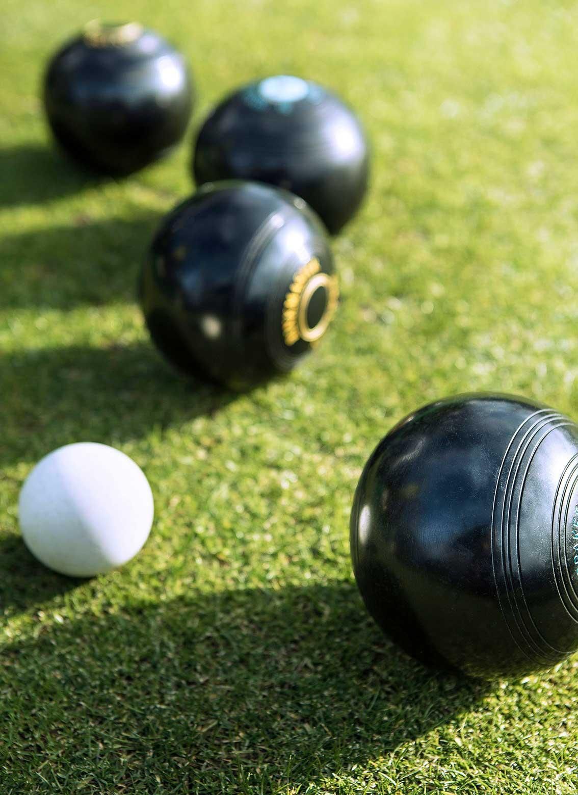 Five black bowling balls and a white ball on green grass.