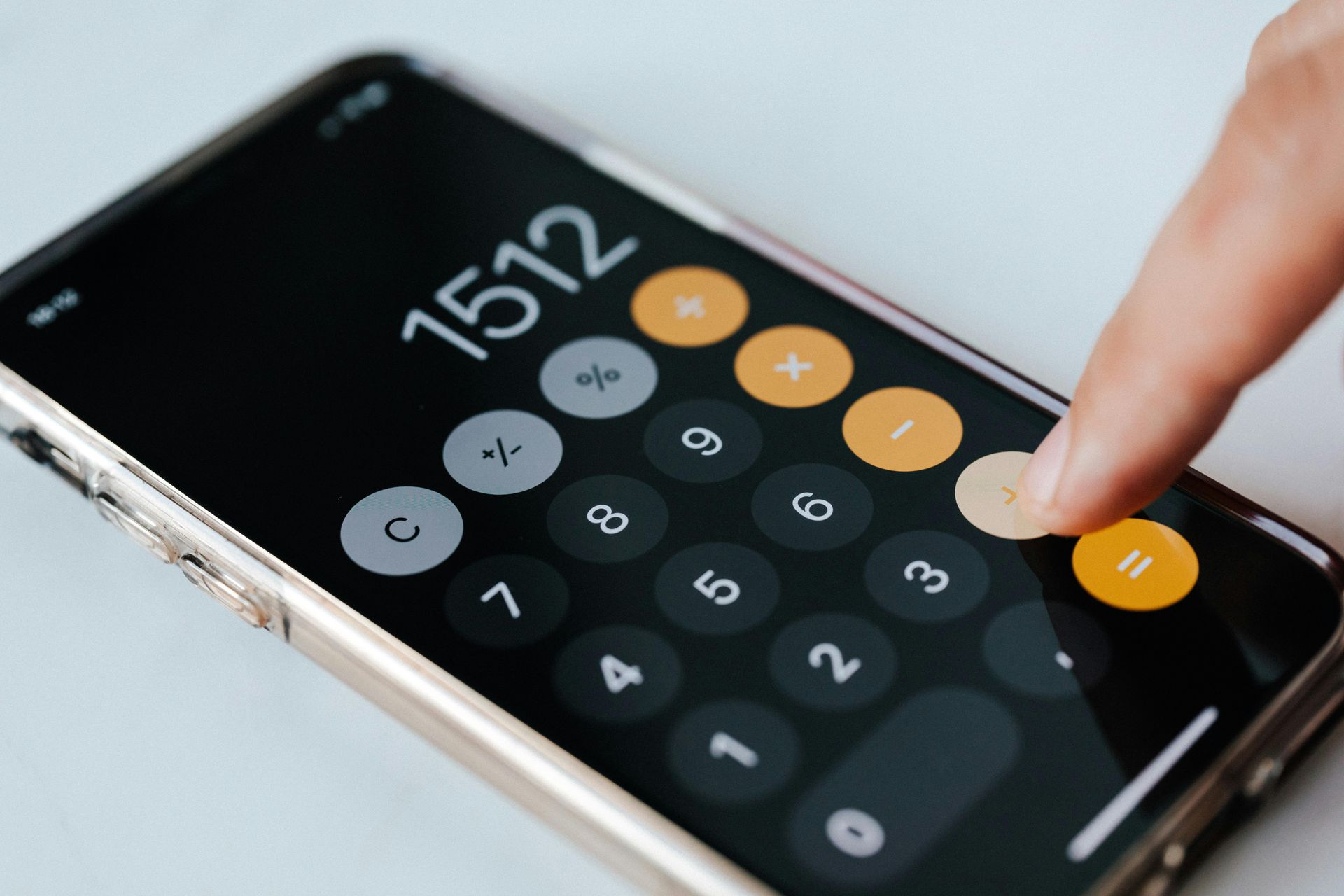A hand pressing the equals button on a calculator app displaying 1512 on a smartphone screen.