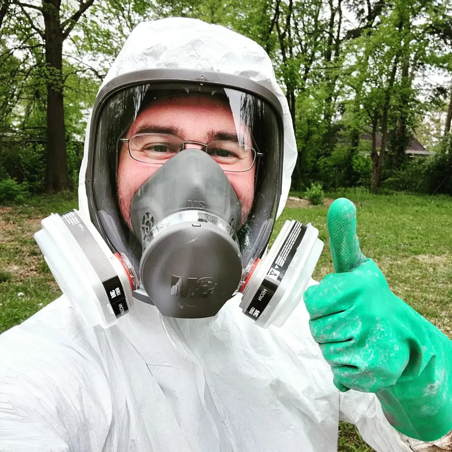 A man wearing a gas mask and gloves is giving a thumbs up.