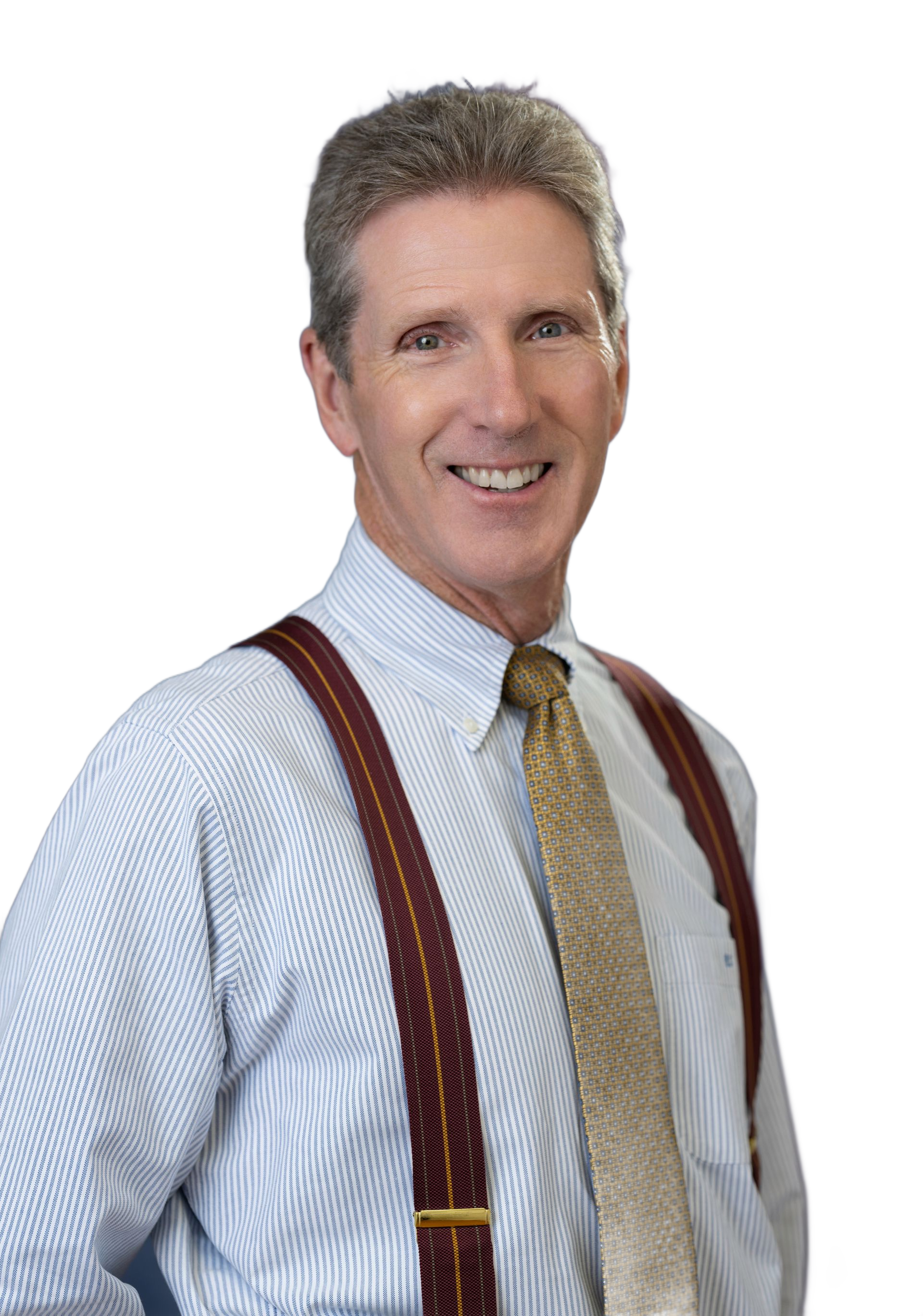 A smiling man with graying hair wearing a white shirt, patterned tie, and suspenders, against a blurred background.