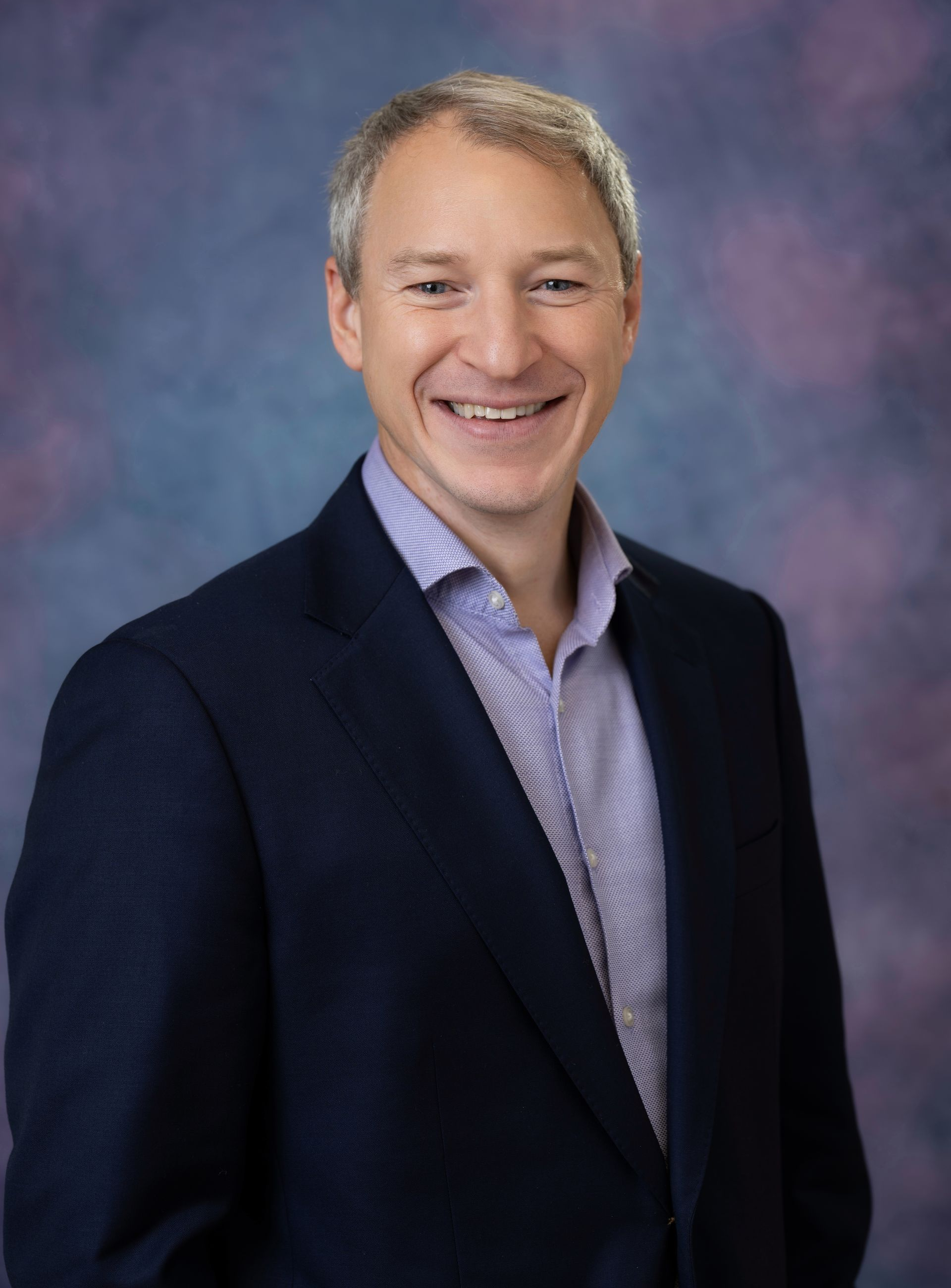 Smiling man in a suit and tie against a black background.