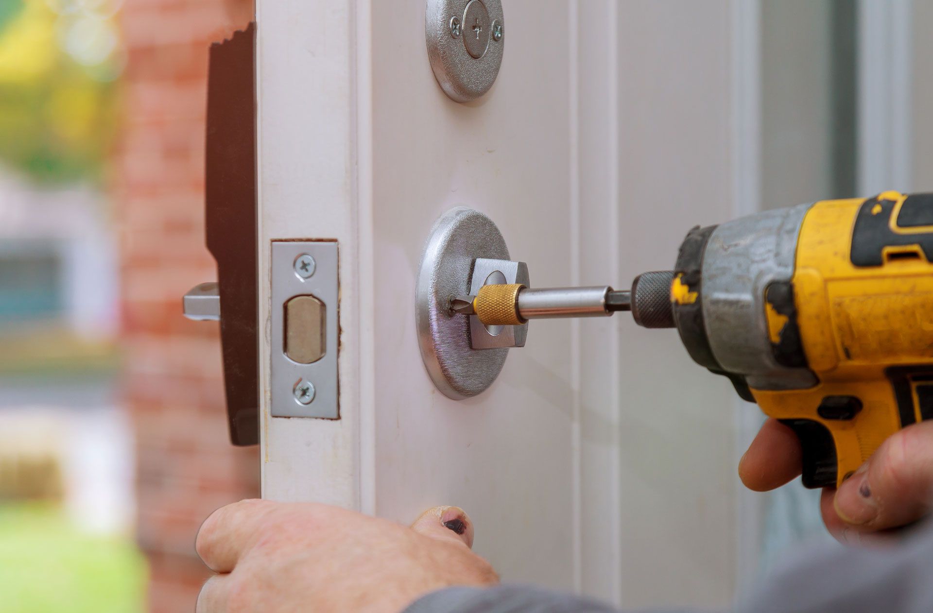 Person using a yellow drill to install a door lock on a white door.