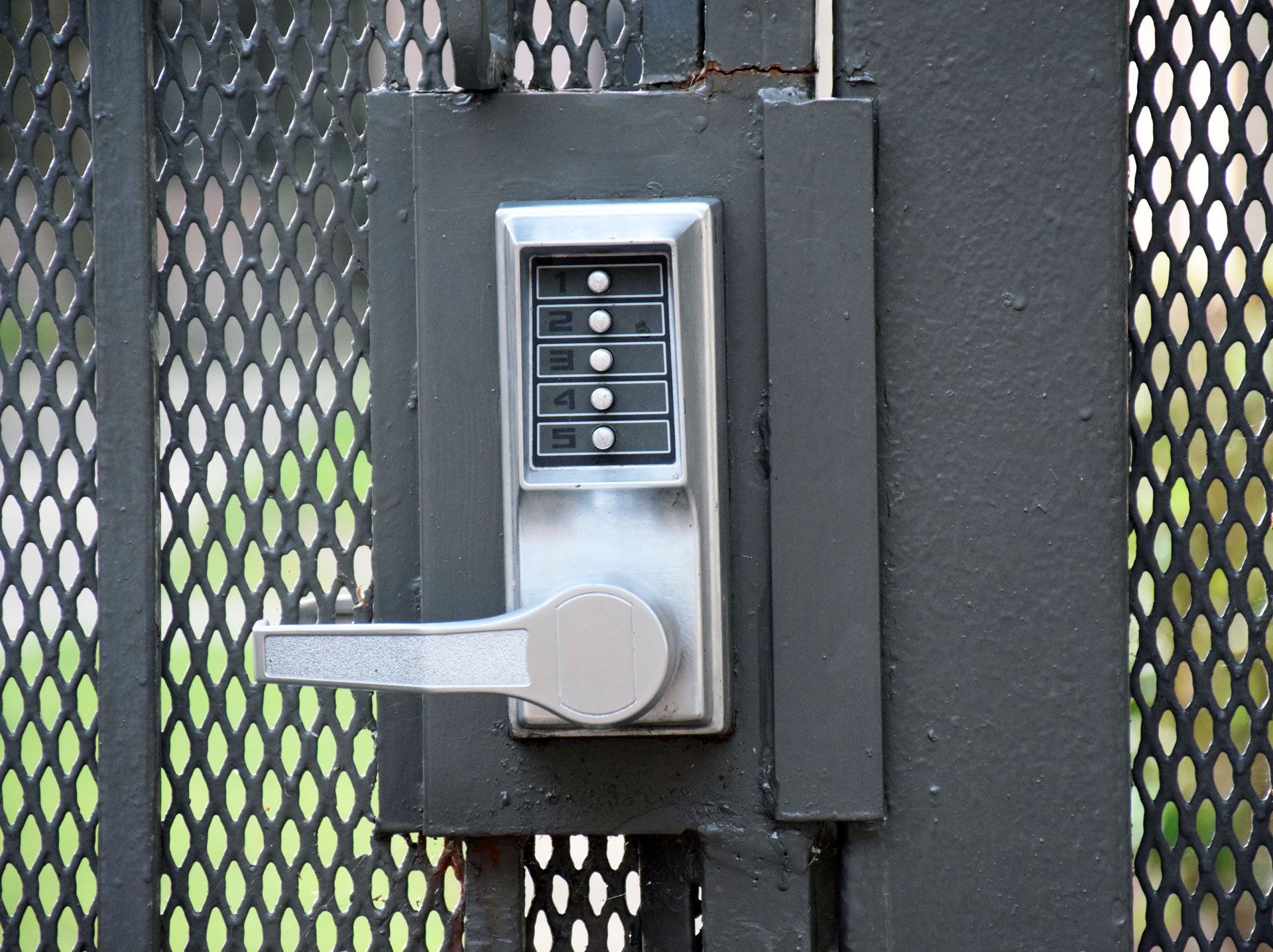 Close-up of a gate with a key code access panel and door handle, both in silver.