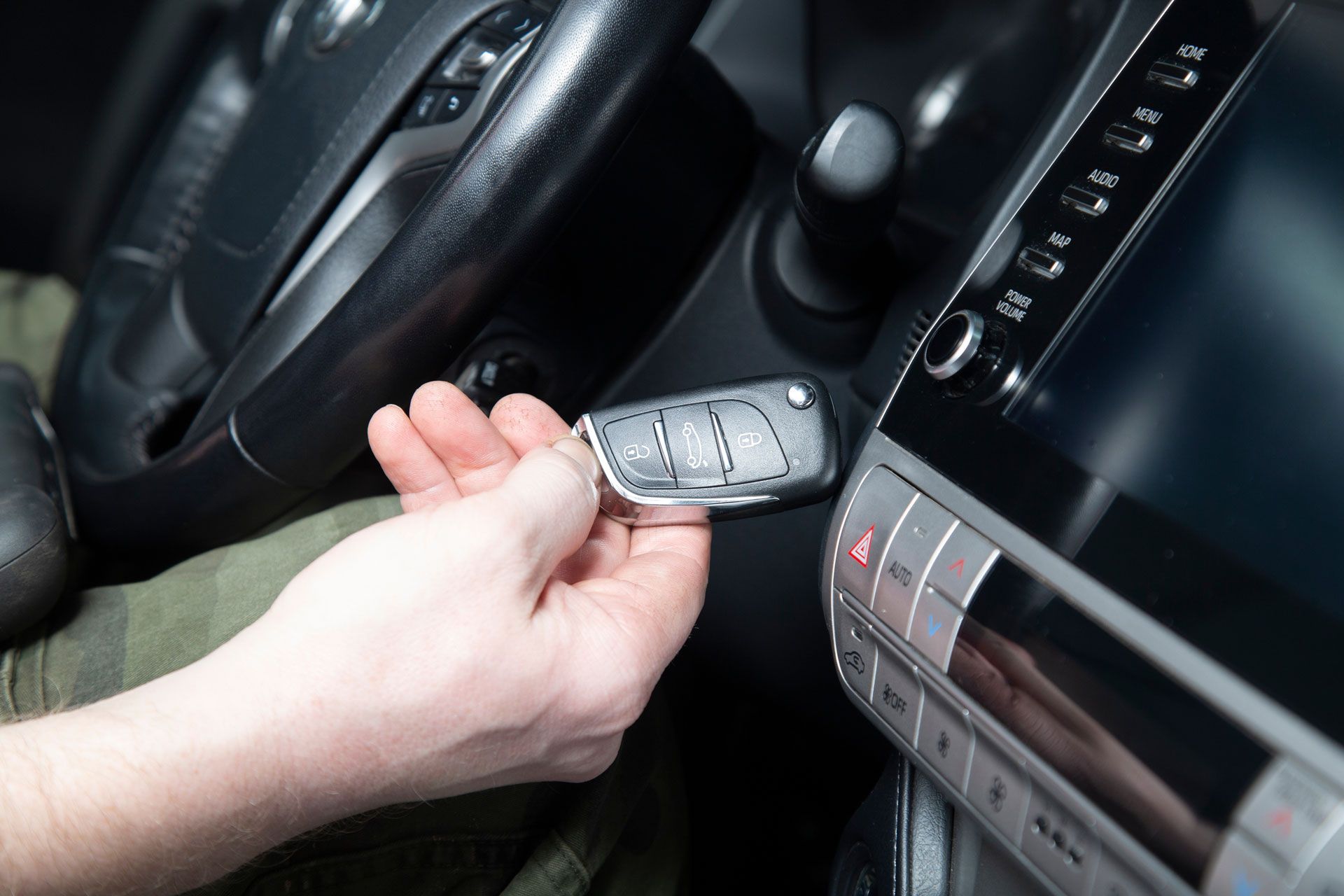 Hand turning a car key in the ignition, near the steering wheel and dashboard.